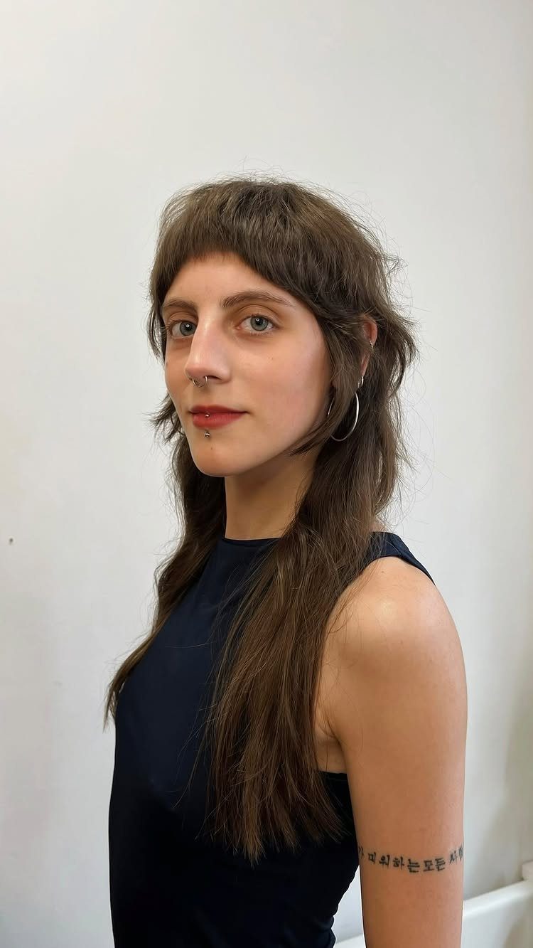 Person posing with long brown shag layers, choppy bangs, and a dark sleeveless top