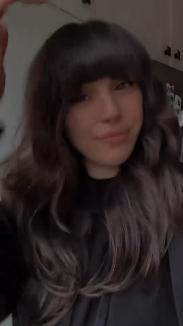 Person with long dark shag haircut, blunt bangs, and layered wavy ends
