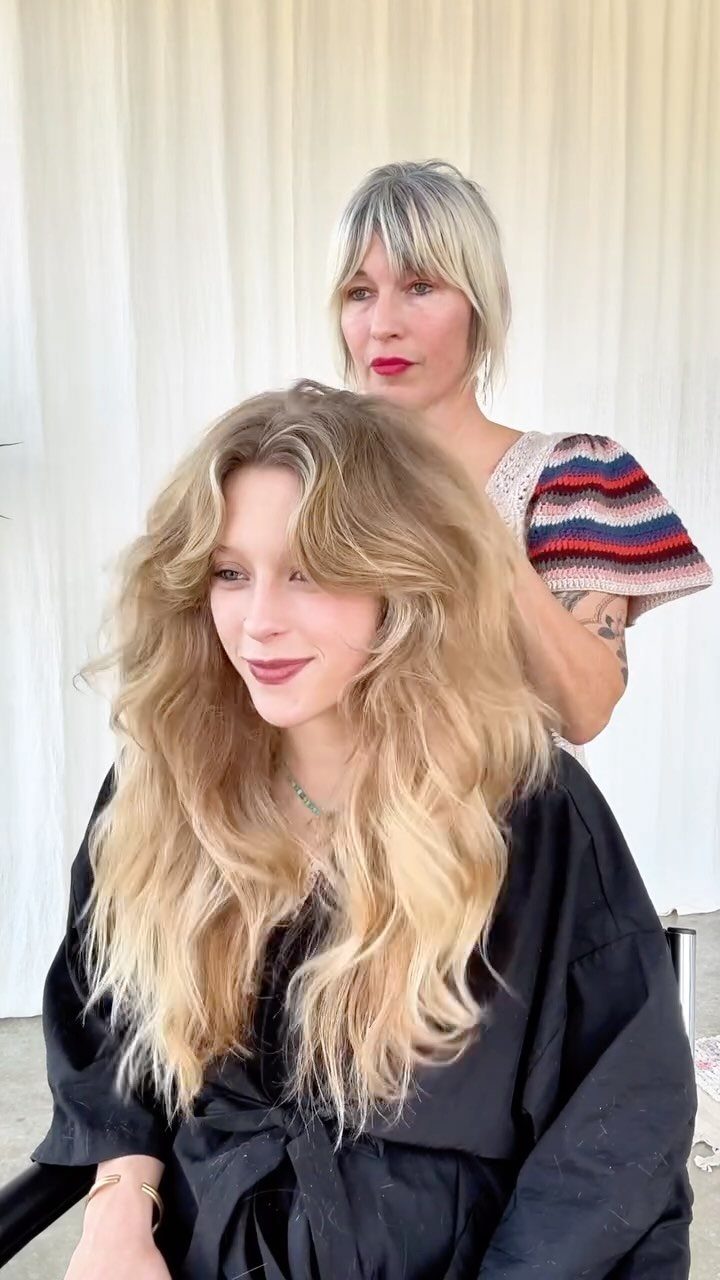 Woman showing long layered blonde hair with parted curtain bangs in a salon
