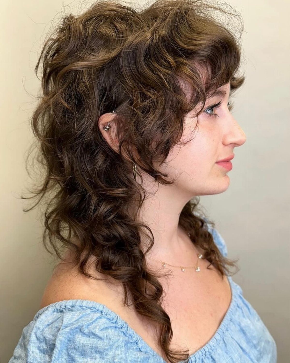 Profile showing a dark, wavy modern mullet shag with short fringe and long curls