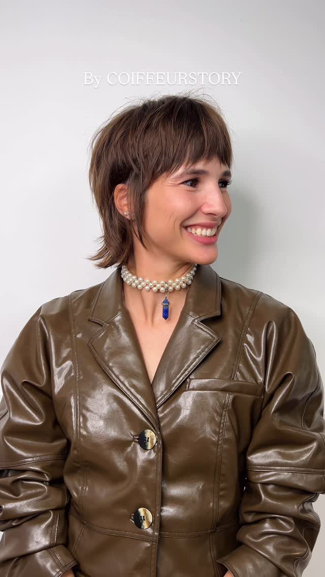 Short layered brown shag with fringe on a smiling person in a leather jacket