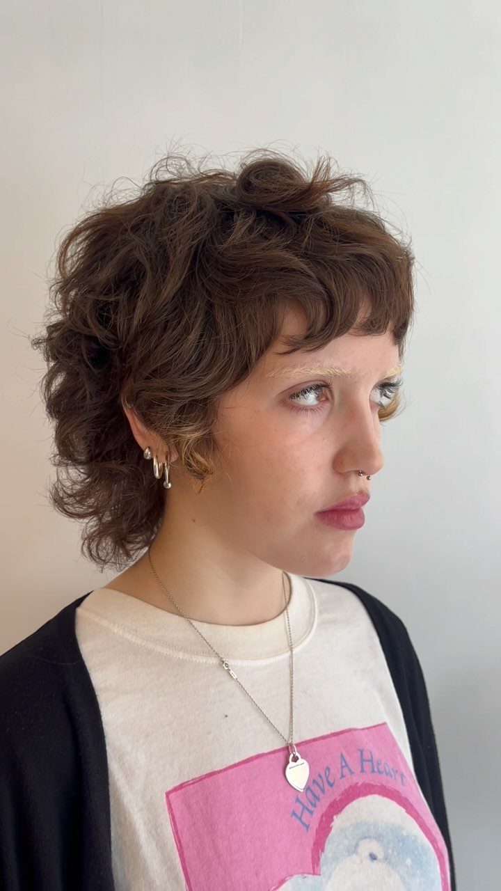 Person with fluffy curly brown pixie haircut shown in side profile