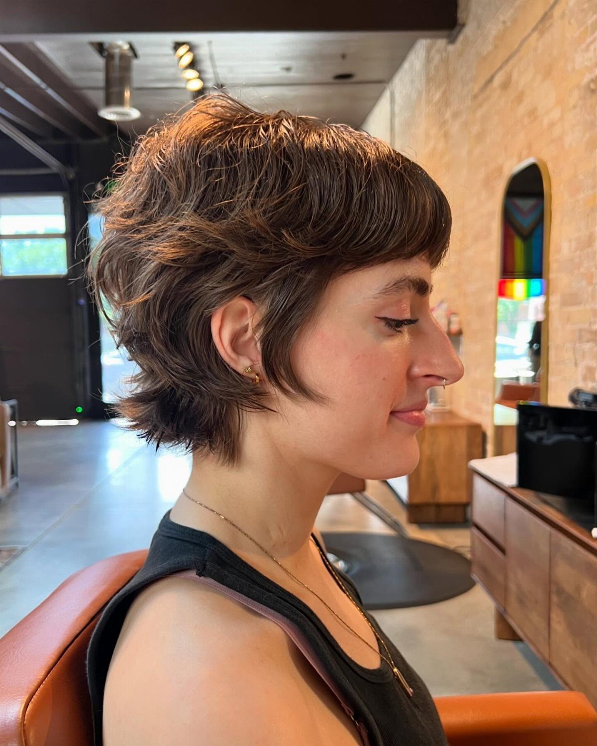 Short brown layered shag with a long fringe, seen in profile at a salon
