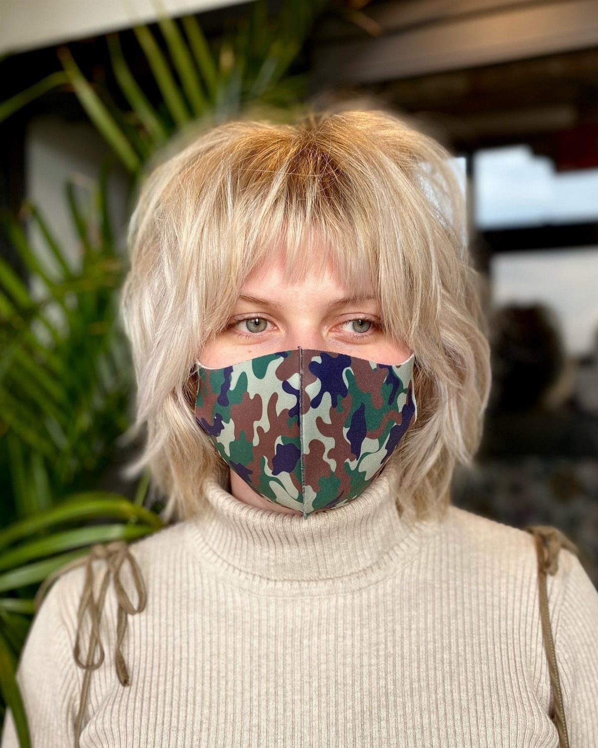 Blonde short shag with wispy layered bangs above a camouflage face mask