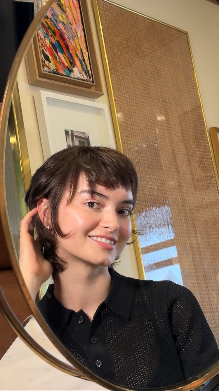 Person showing short shaggy haircut with straight blunt bangs in an oval mirror