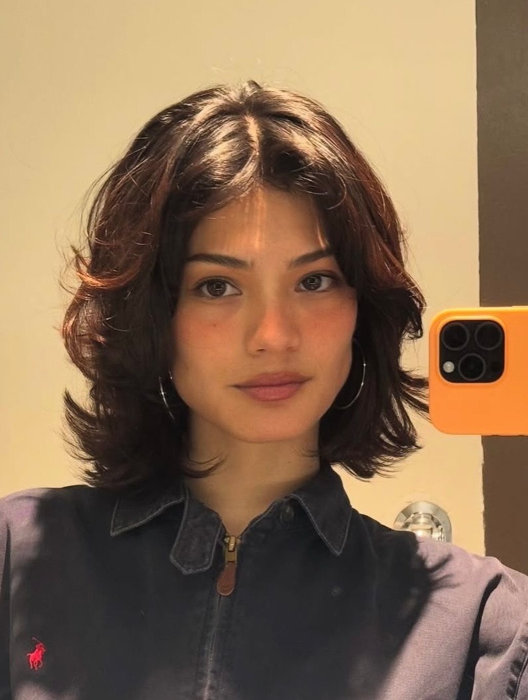 Woman with a center-parted short shag haircut taking a mirror selfie