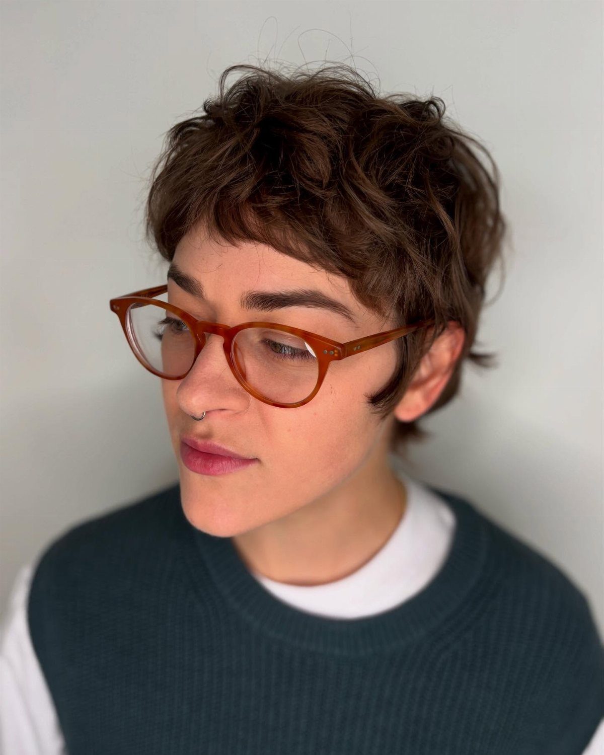 Person with a voluminous, tousled dark pixie shag and tortoiseshell glasses