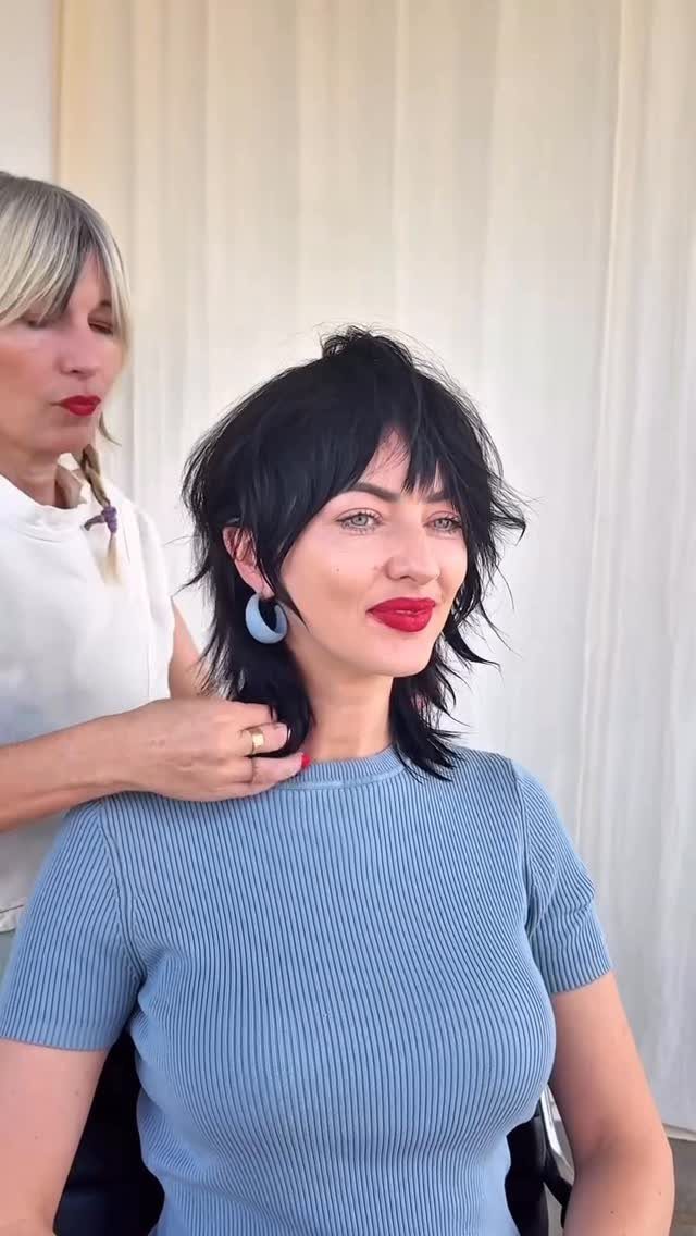 Woman models a short black shag with wispy bangs as a stylist adjusts her layers
