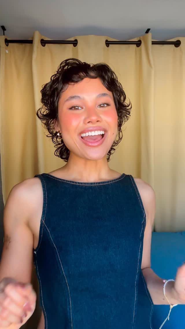 Short dark curly pixie shag with choppy layers frames a smiling person's face