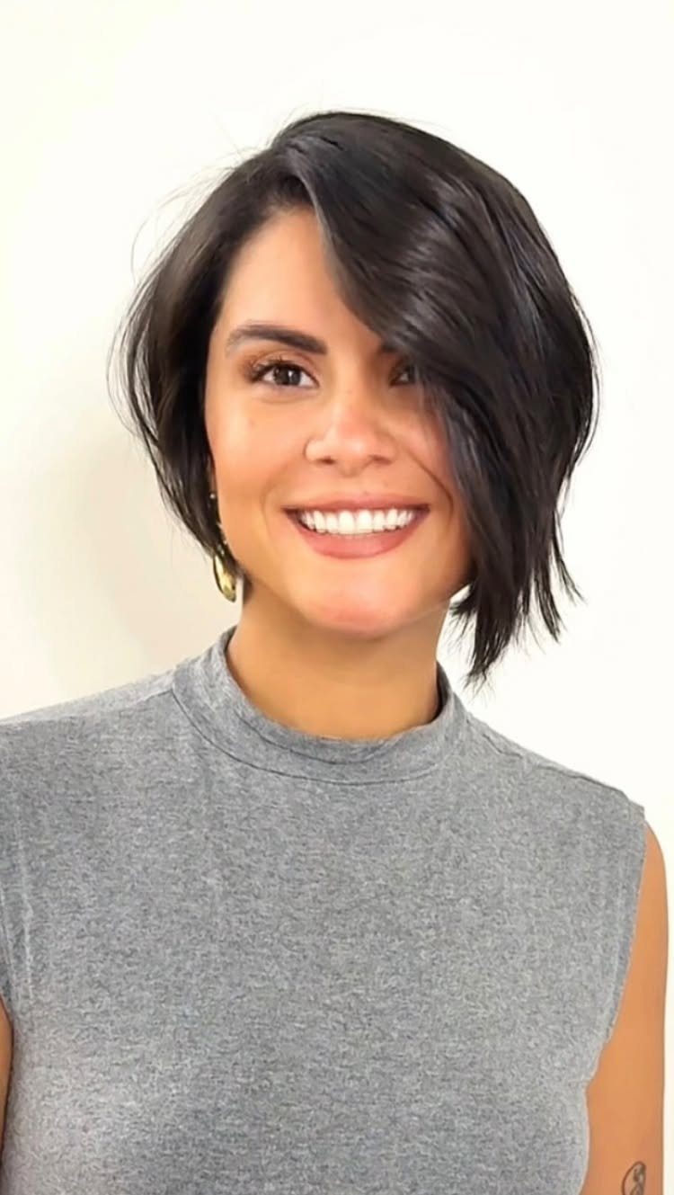 Smiling woman showcasing a dark asymmetrical short haircut with sweeping longer side