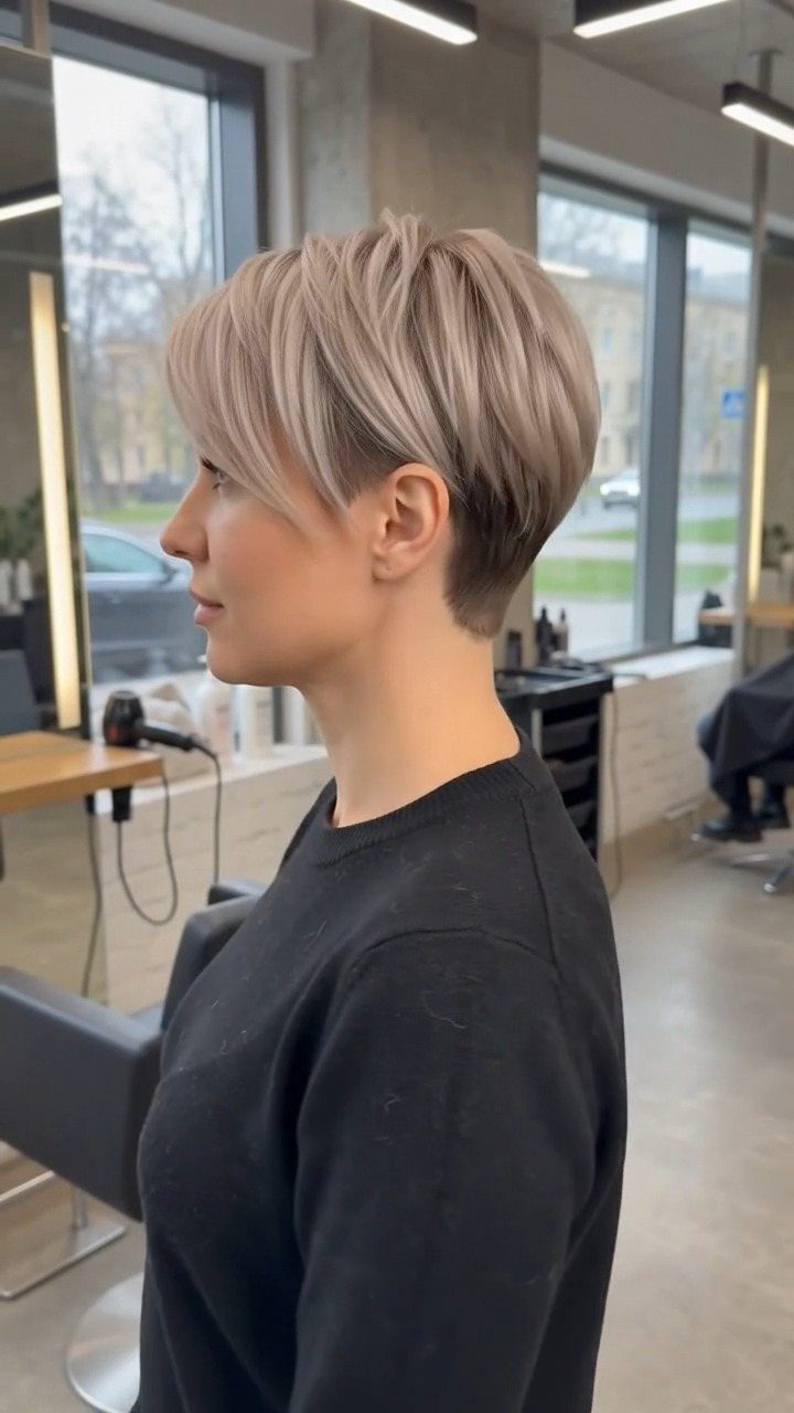 Silver-blonde pixie haircut with feathered layers and wispy bangs in a salon
