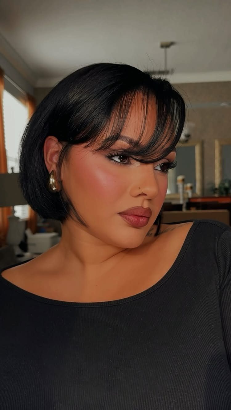 Woman with a short dark bob and wispy bangs posing indoors