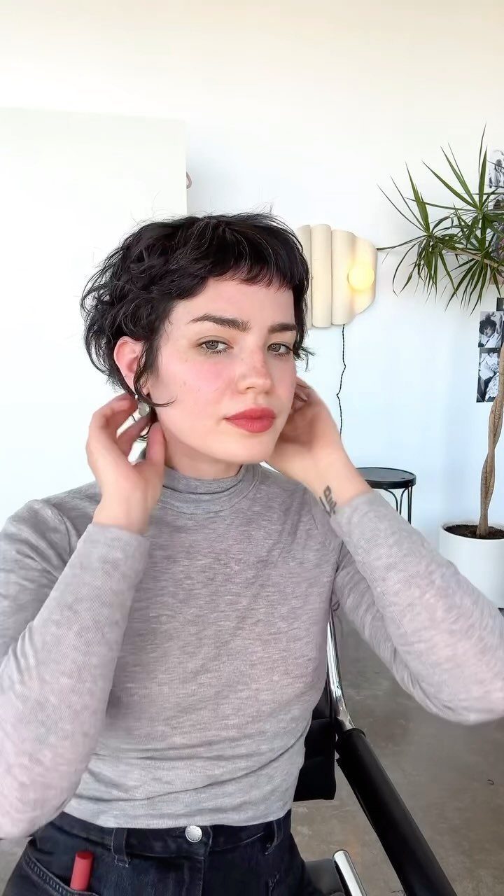 Person showing a short dark piece-y pixie haircut indoors