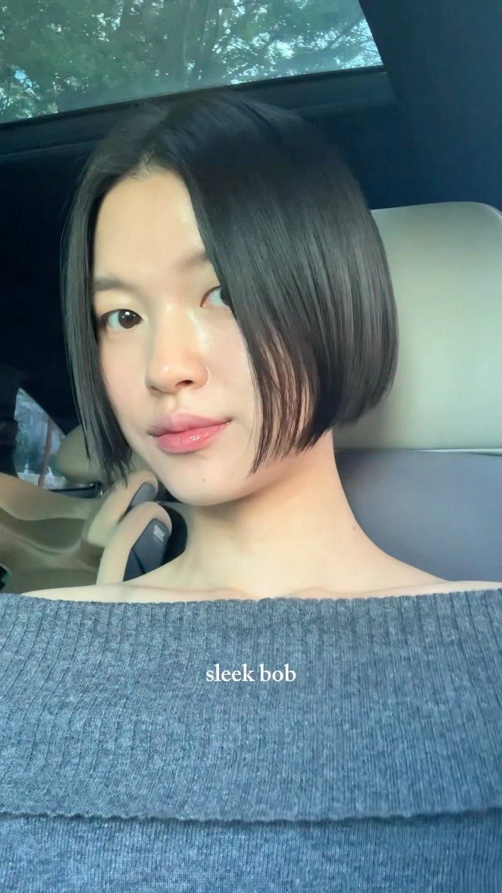 Person with a smooth, straight black bob seated inside a car