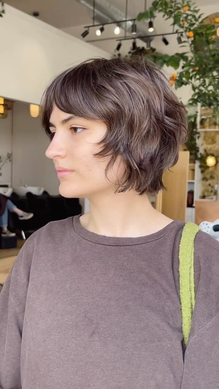Textured dark brown bob with wispy bangs shown in side profile at a salon