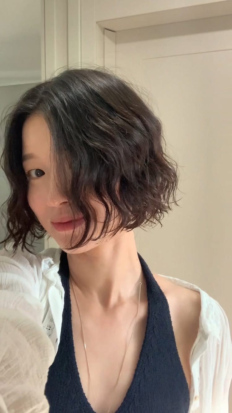 Person wearing a short, dark, wavy bob with loose strands framing the face