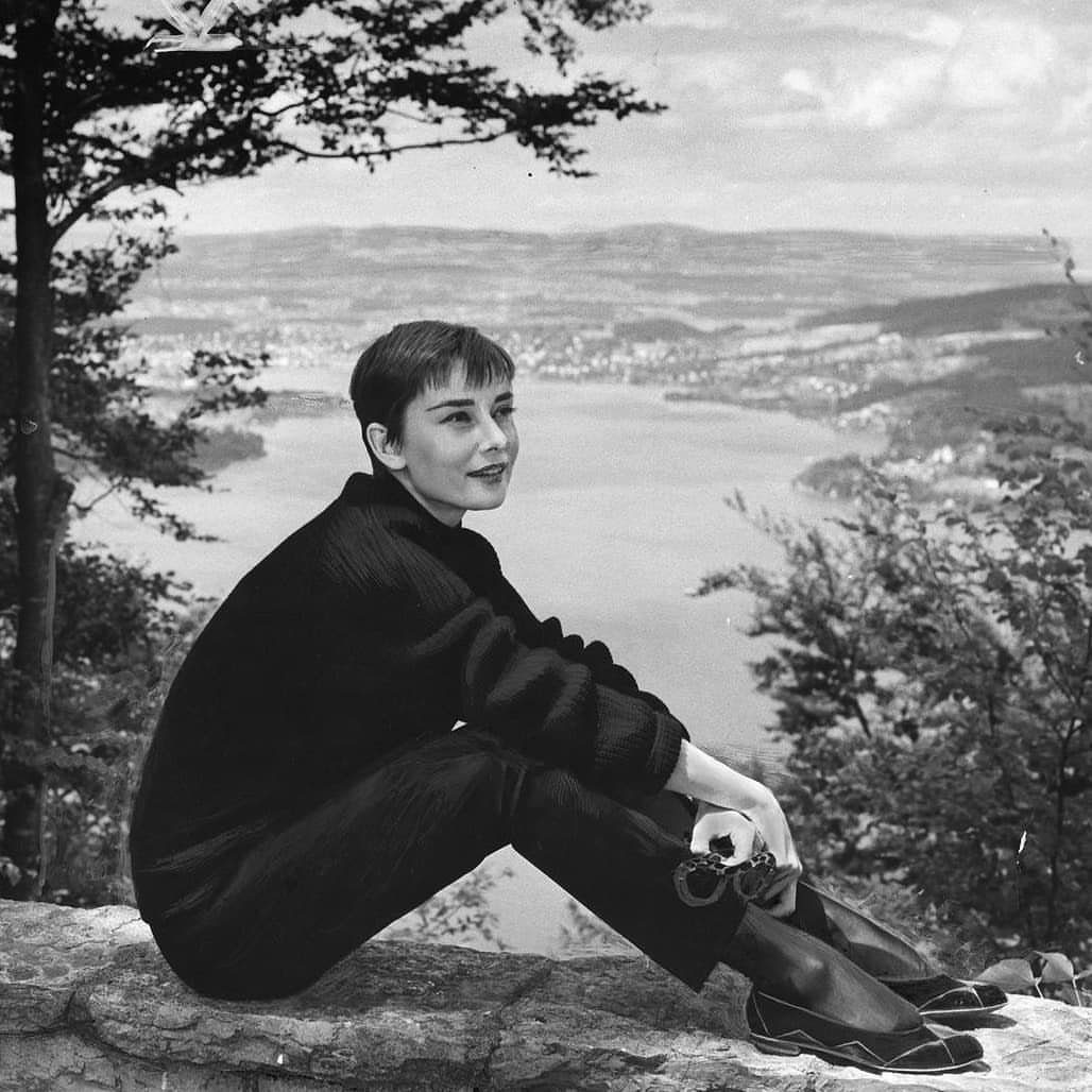 Woman with a softly framed short pixie cut sitting on a stone ledge