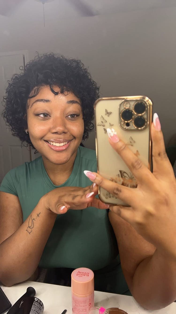 Woman with short curly pixie hair smiles while taking a bathroom mirror selfie