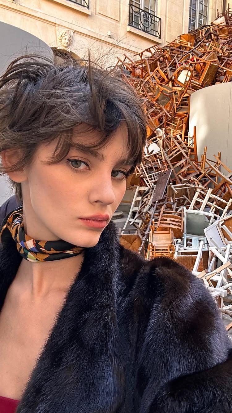 Person with tousled dark pixie hair and wispy bangs in a black coat