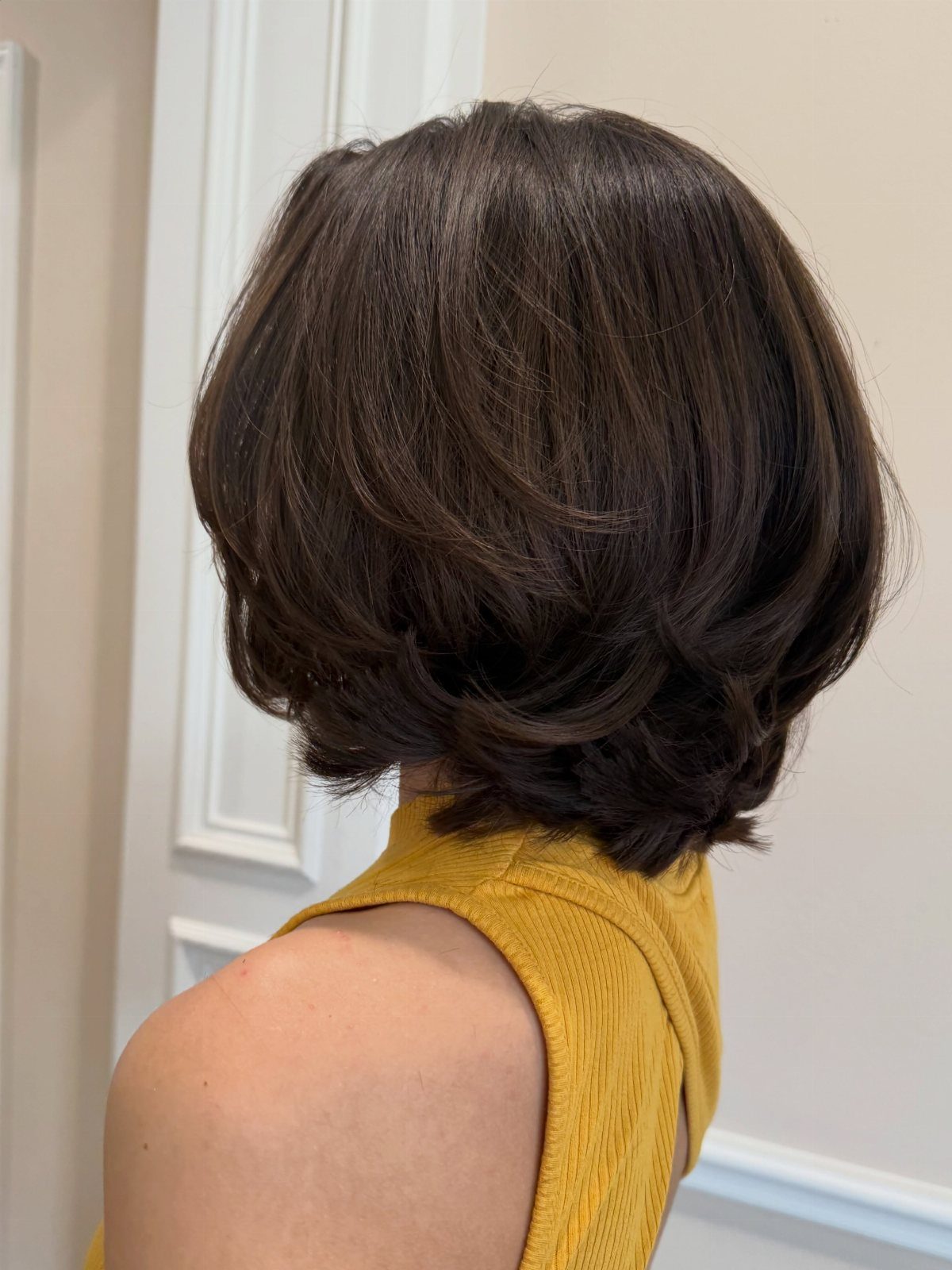 Short dark layered bob with rounded bouncy ends on person in mustard top