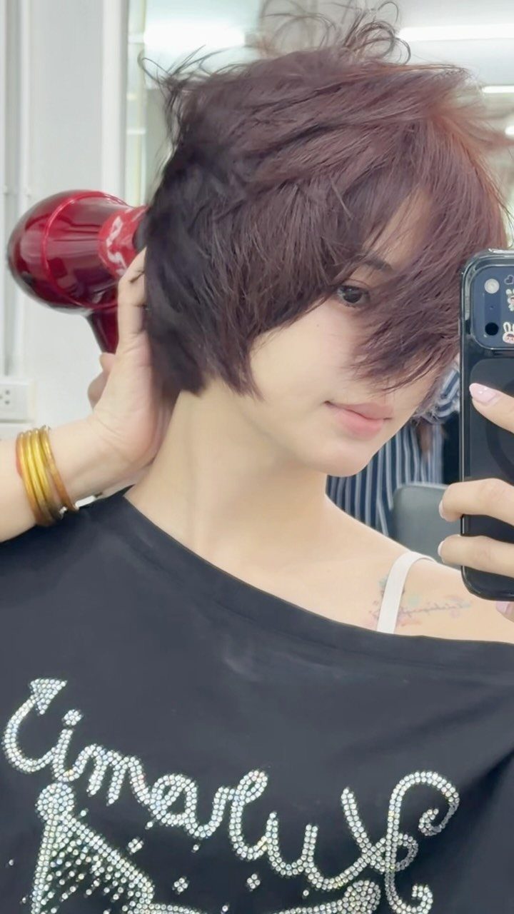 Person showing a tousled, choppy dark pixie haircut in a mirror