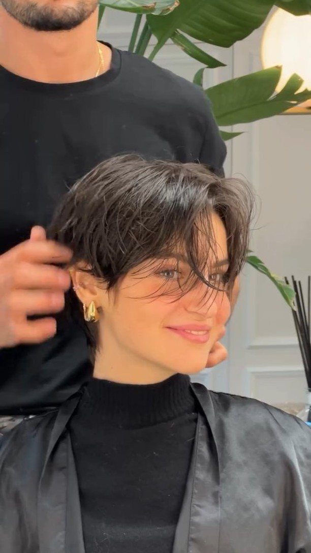 Woman showing a long, layered dark pixie cut with side-swept bangs in a salon