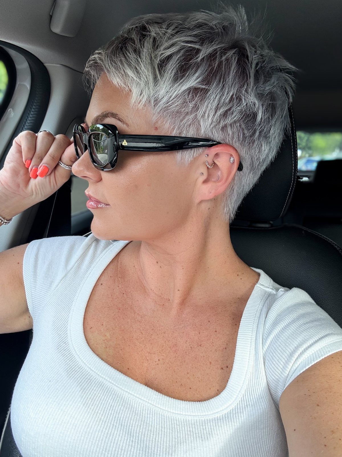 Woman showing a choppy natural silver pixie haircut in a car