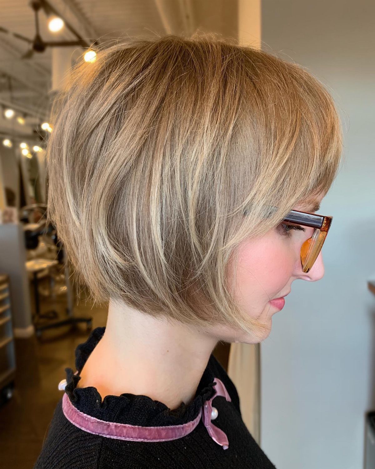 Woman with a wispy, layered blonde bob and glasses in a salon