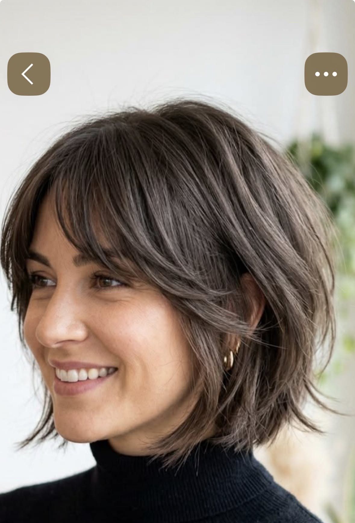 Woman smiling in a sliced dark bob with gray highlights and side-swept bangs