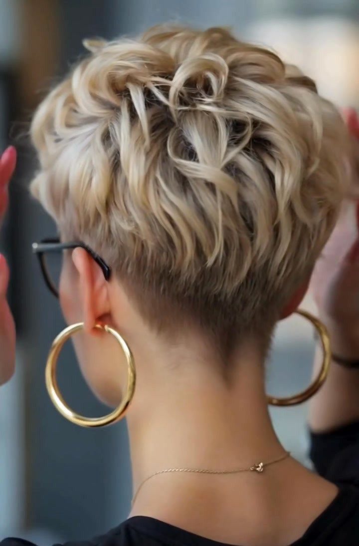 Tousled blonde pixie with short tapered hair at the nape and gold hoop earrings