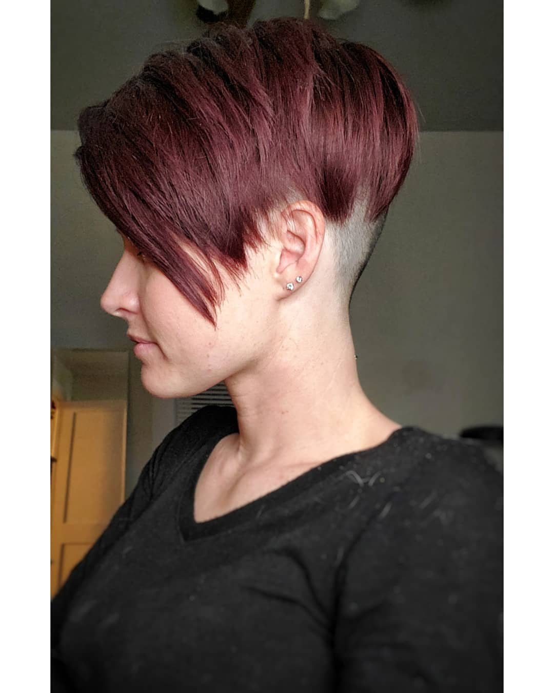 Side-profile person showing a voluminous burgundy undercut pixie with feathered layers