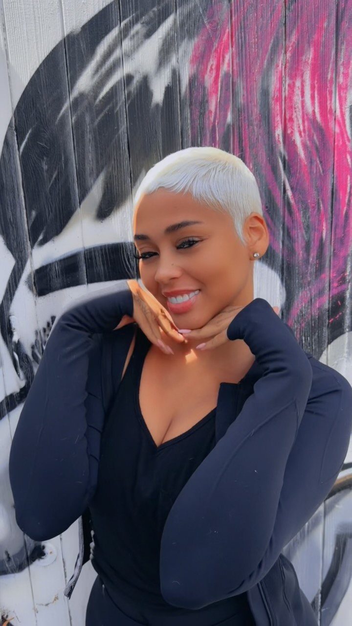 Woman with a short platinum-blonde pixie cut posing against a graffiti wall
