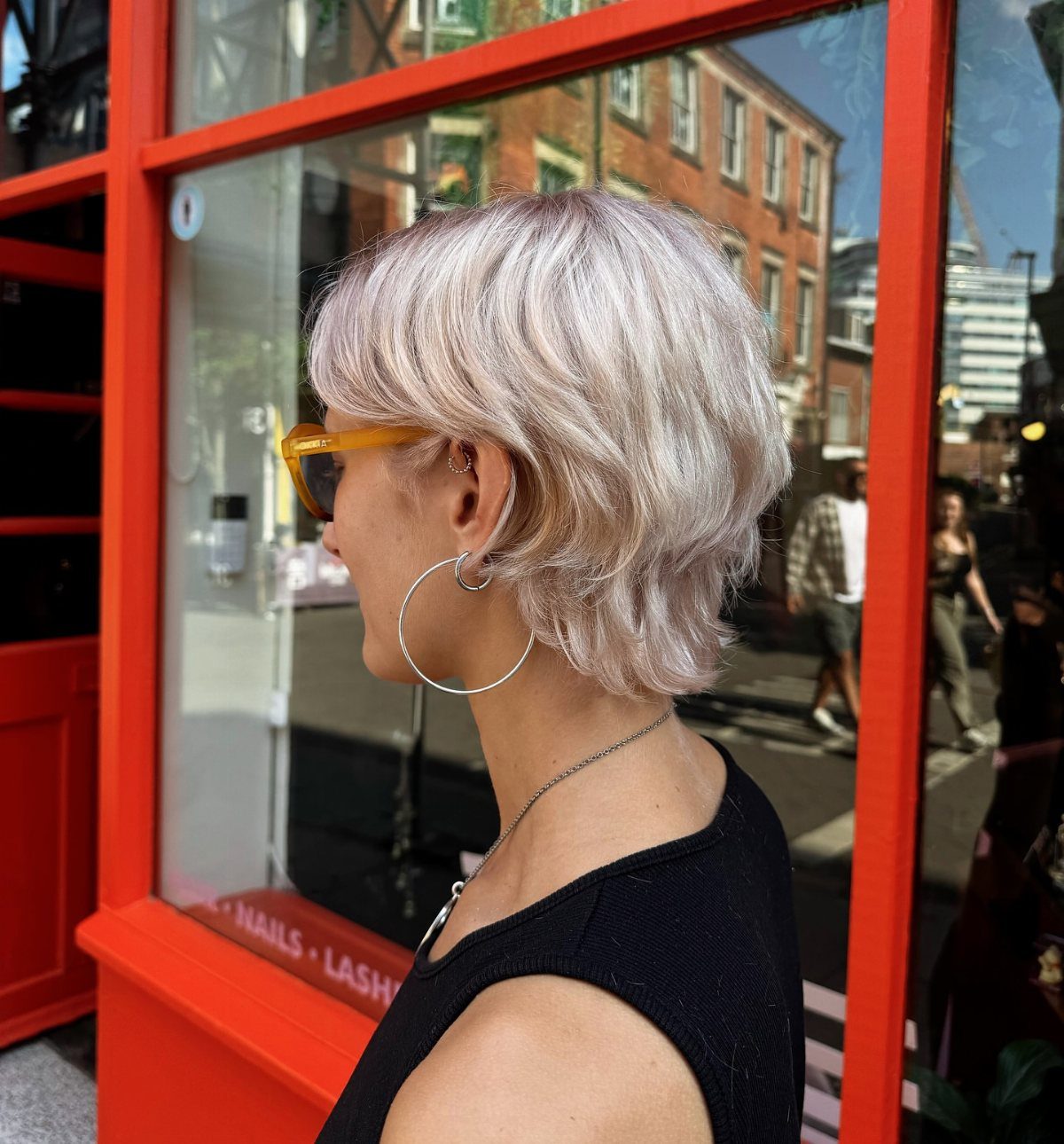 Silver-blonde grown-out pixie with wispy bangs shown in profile beside a storefront