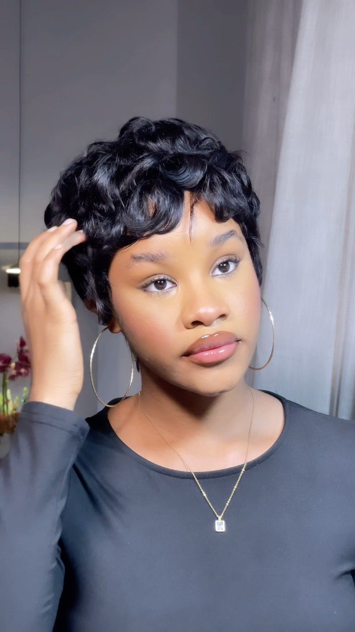 Woman touching her short, layered black pixie cut with wavy side-swept fringe