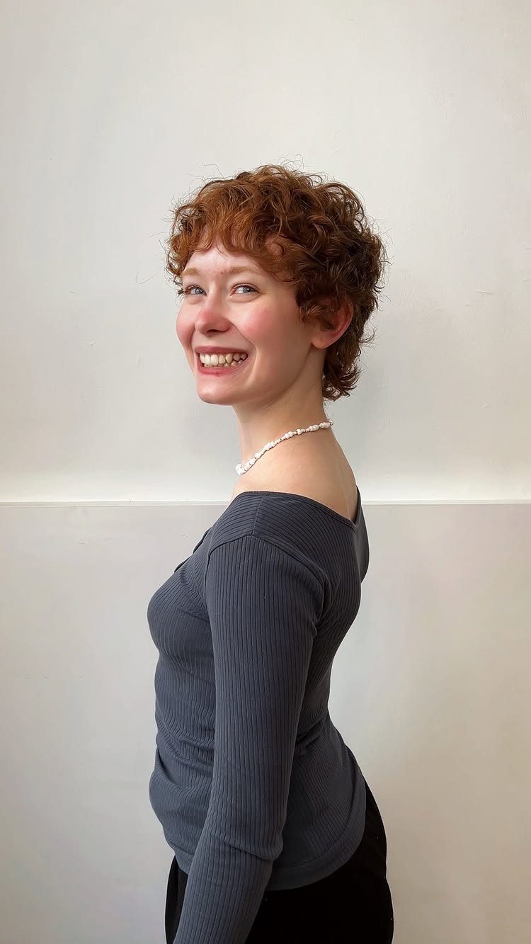 Woman showing a short, shaggy reddish-brown pixie with tousled curls