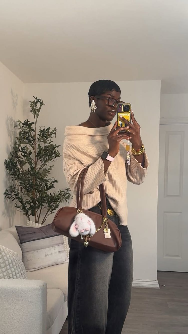 Person with closely cropped dark hair takes a mirror selfie in a cream sweater