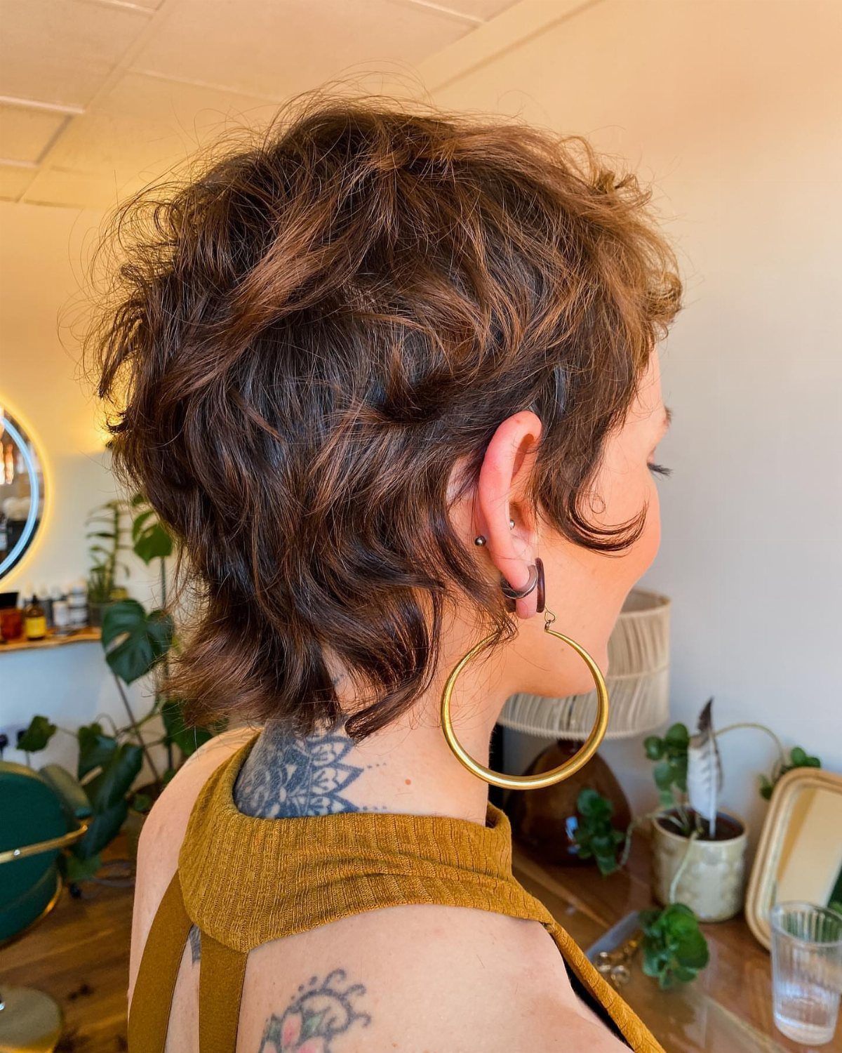Short wavy pixie cut shown from behind, with dark tousled hair and a gold hoop earring
