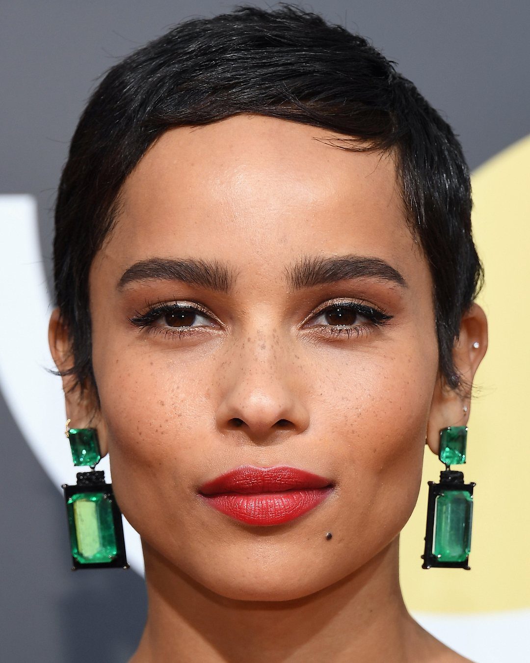 Woman with a neat, short black pixie cut and large green earrings