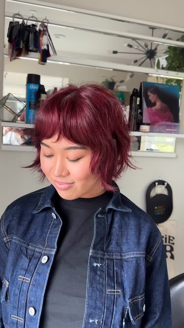 Layered burgundy shag bob with wispy bangs in a salon
