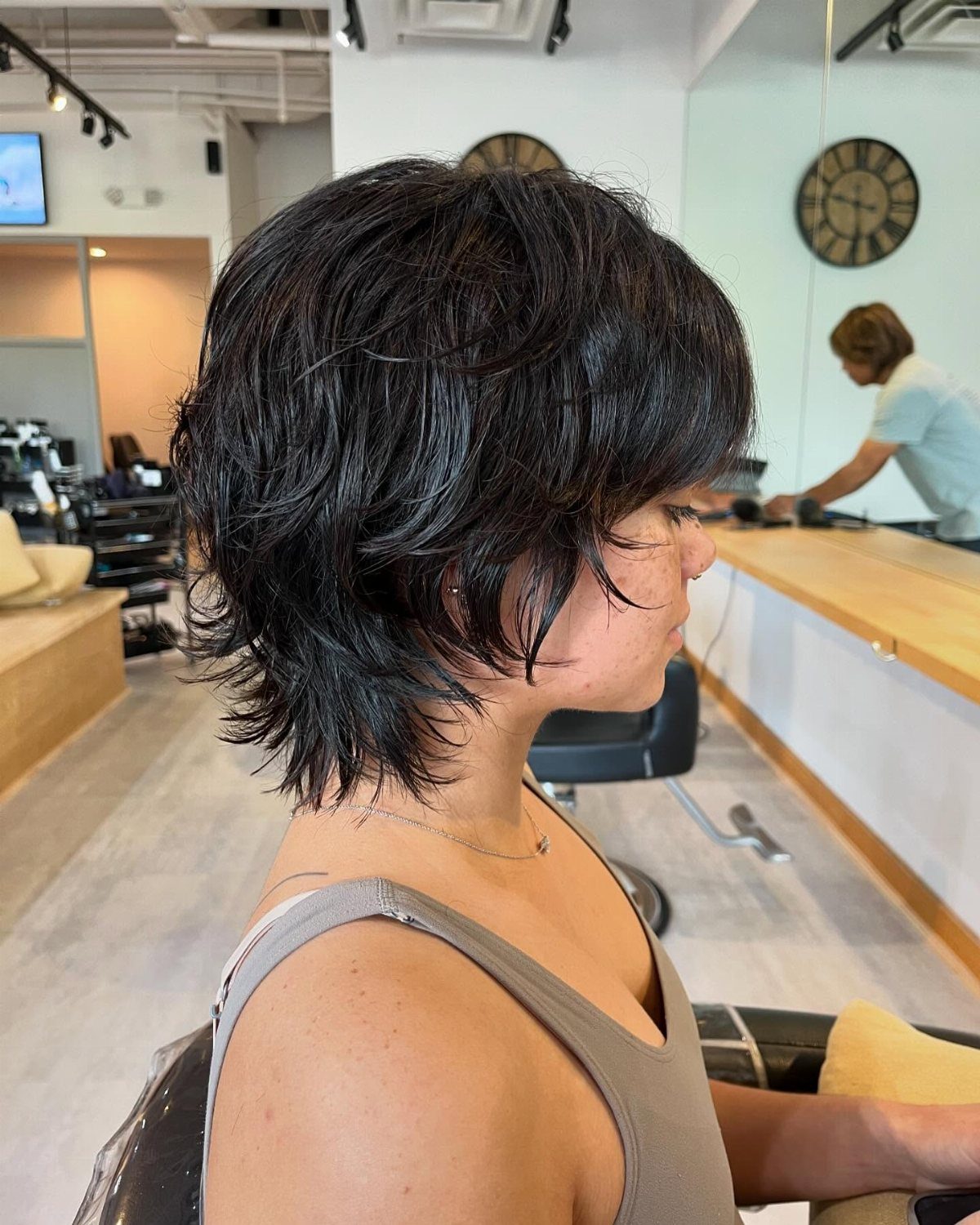 Short dark modern mullet with shaggy layers shown in profile at a salon