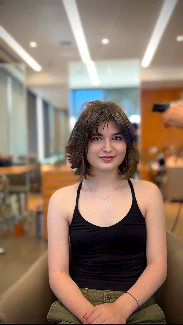 Woman with a rounded brown shag haircut and wispy bangs in a salon