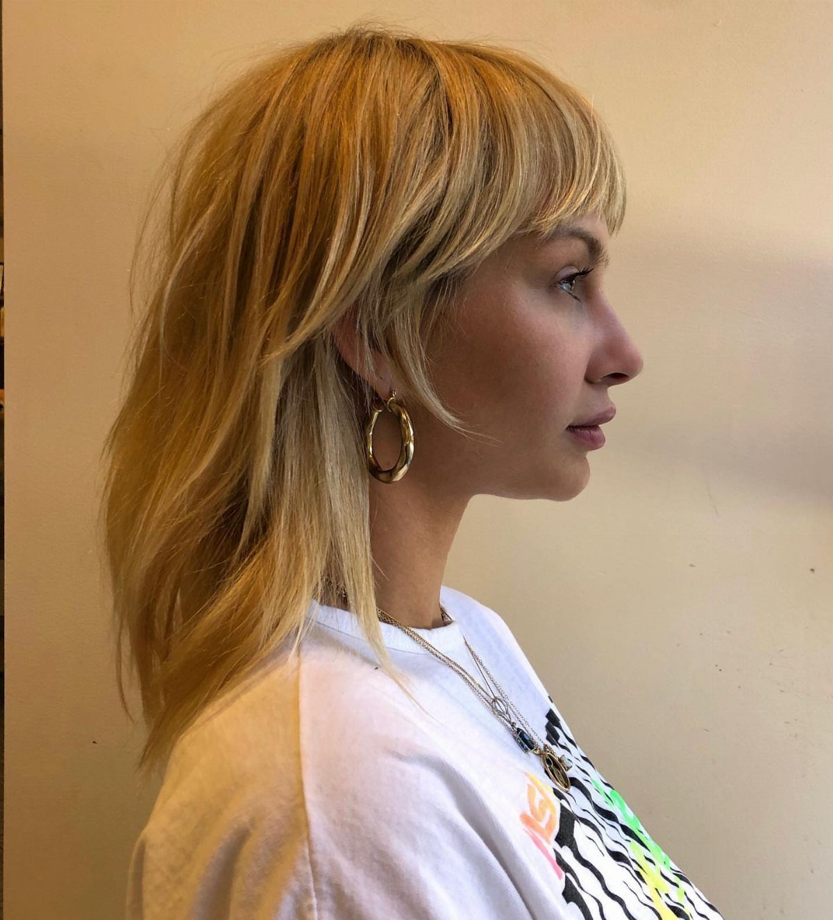 Blonde woman with long layered shag haircut and full bangs in profile