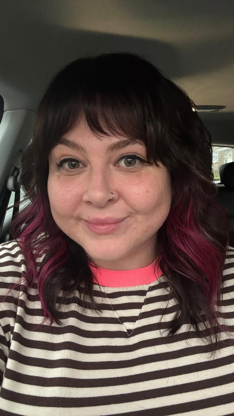 Woman with a short dark shag haircut and wispy bangs in a car