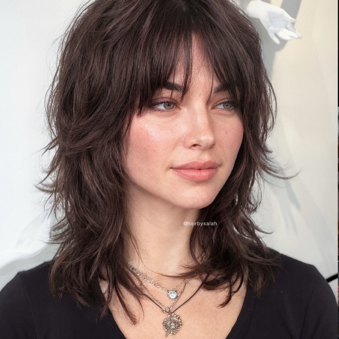 Woman with dark brown wispy shag haircut and feathered shoulder-length layers