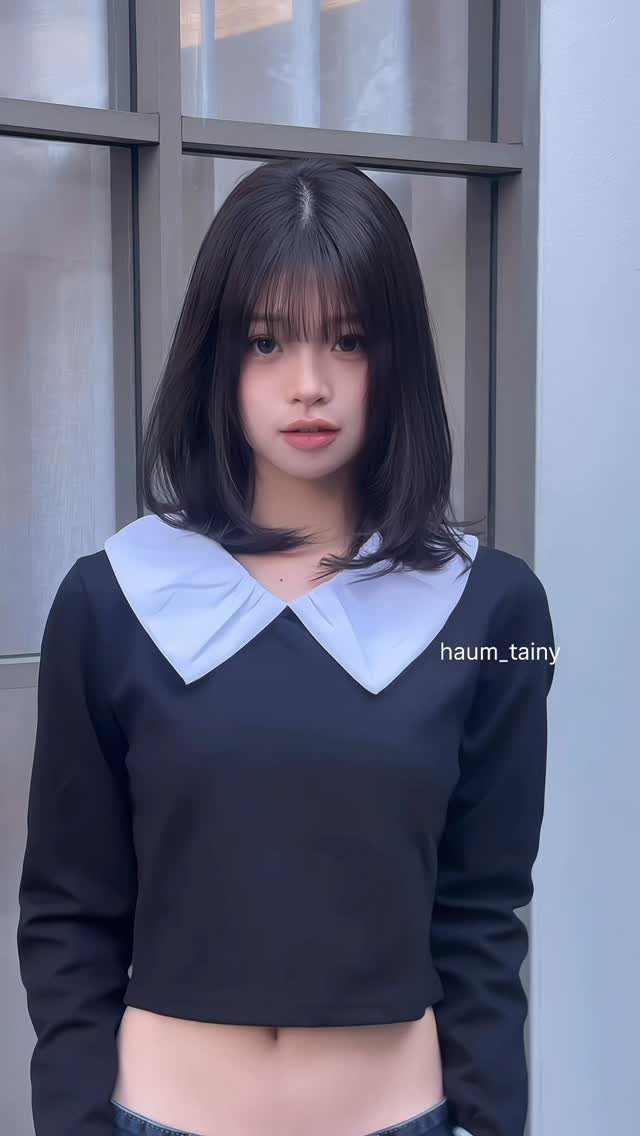 Woman with a shoulder-length black bob and wispy bangs standing before a window
