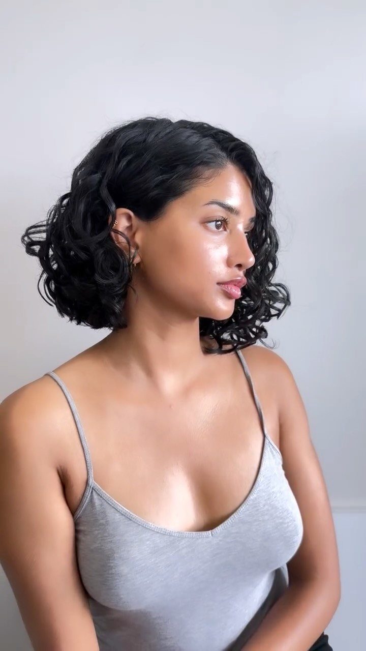 Woman with a dark shoulder-length curly bob, shown in profile against a light background