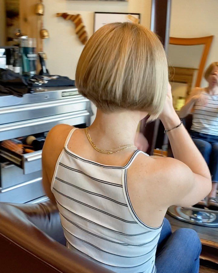 Blonde inverted bob with a short rounded nape, viewed from behind in a salon