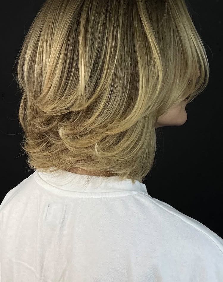 Blonde layered bob with feathered, outward-curving ends against a dark background