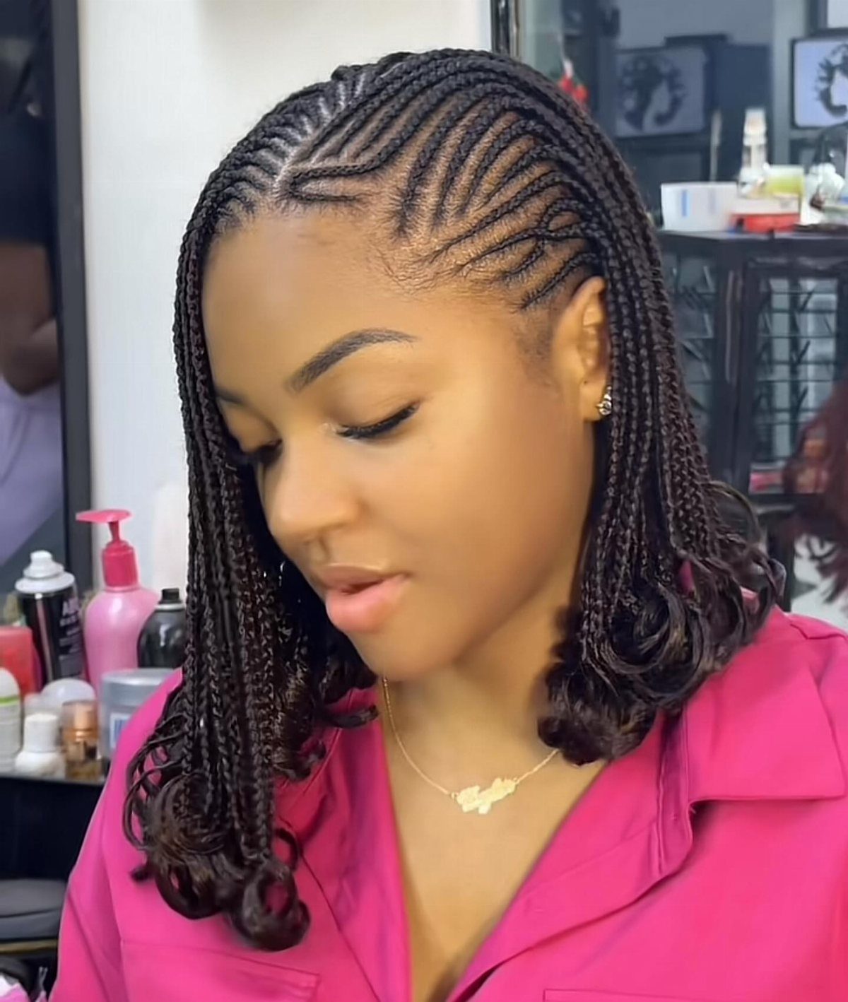 Side-parted cornrow braids with curled ends frame a woman's face in a salon