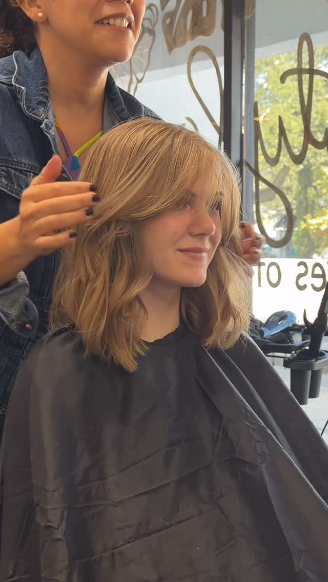 Shoulder-length brown hair styled with center-parted curtain bangs in a salon
